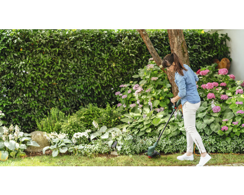 Femme coupant l''herbe avec un coupe-bordures dans un jardin avec des fleurs et des arbustes.
