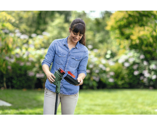 Une femme fixe un bac de ramassage de l''herbe sur un coupe-bordure dans le jardin.