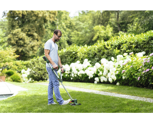 Un homme coupe du gazon avec un coupe-bordure dans le jardin.