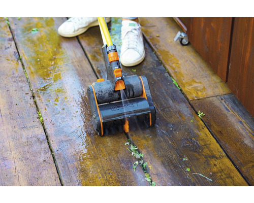 Eine Person reinigt eine Holzterrasse mit einer Bürste und Wasser.