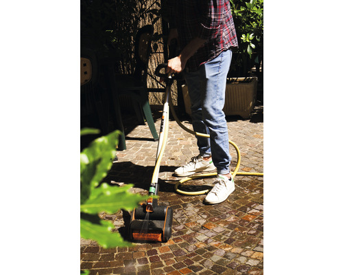 Mann reinigt Pflastersteine mit einem Terrassenreiniger und Wasserschlauch im Garten