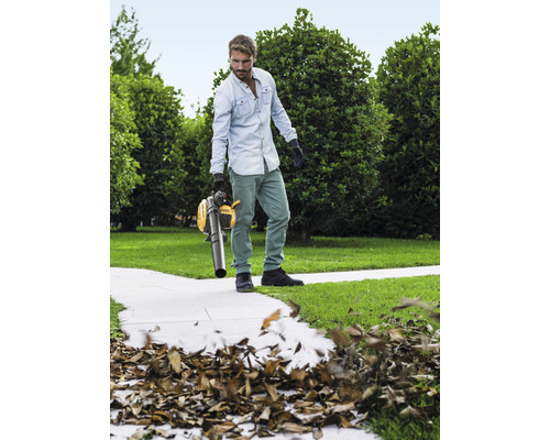 Un homme utilise un aspirateur à feuilles jaune dans le jardin pour enlever les feuilles.
