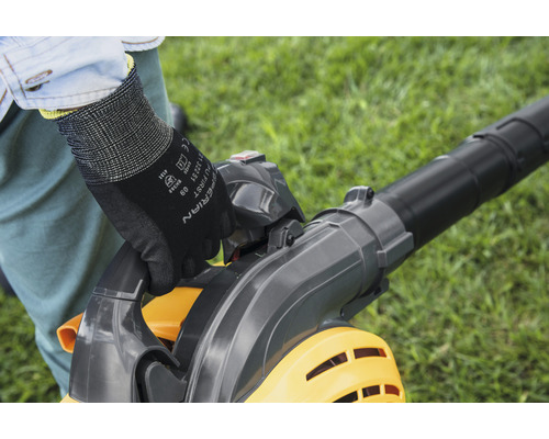 Une personne utilise un aspirateur à feuilles dans le jardin et porte des gants.