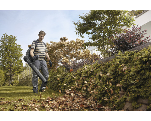 Un homme utilise un souffleur de feuilles dans le jardin pour enlever les feuilles.