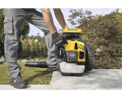 Un homme utilise un souffleur de feuilles Stiga jaune dans un jardin.