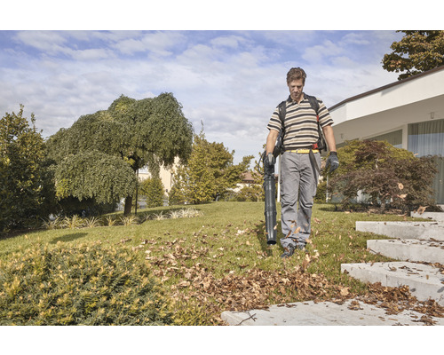 Un homme utilise un aspirateur à feuilles dans le jardin pour enlever les feuilles.