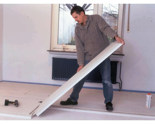 Un homme installe une plinthe dans une pièce.