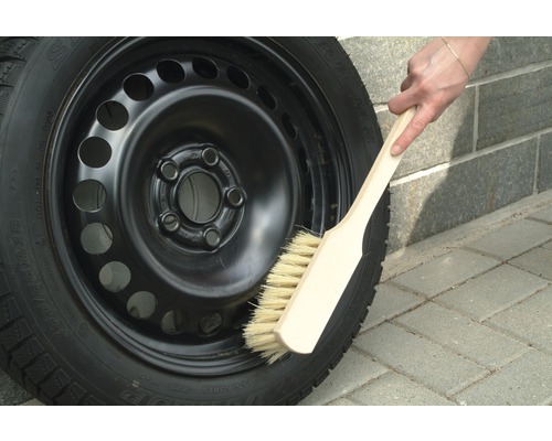 Une jante en acier avec un pneu d''hiver est nettoyée avec une brosse.