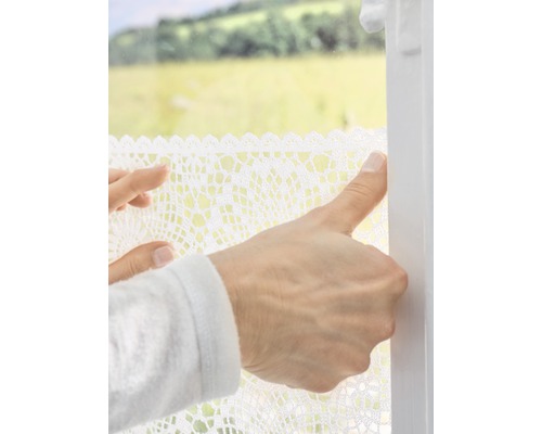 Une personne fixe un film de fenêtre avec de la dentelle au crochet sur la fenêtre