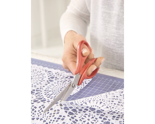 Une personne coupe de la dentelle blanche avec des ciseaux sur un tapis de découpe.