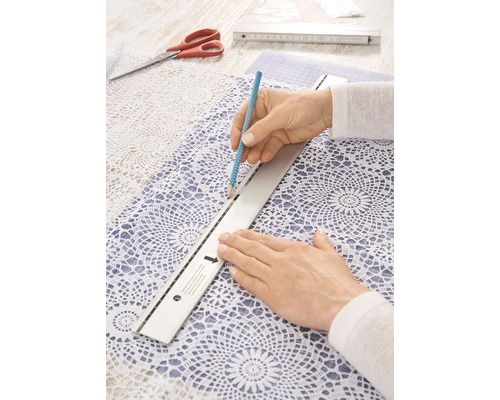Personne dessinant avec un crayon et une règle sur une nappe en dentelle