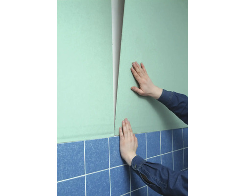 Une personne fixe une plaque de plâtre sur un mur au-dessus de carreaux.