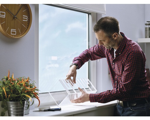 Ein Mann montiert einen transparenten Fensterschutz in einem Innenraum.
