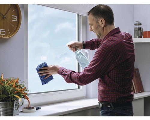 Mann putzt Fenster mit Sprühflasche und Tuch