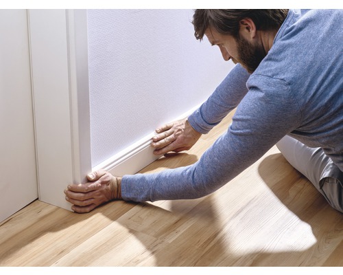 Un homme installe une plinthe sur un mur