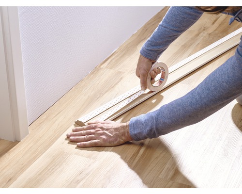 Une personne fixe du ruban adhésif sur une plinthe.