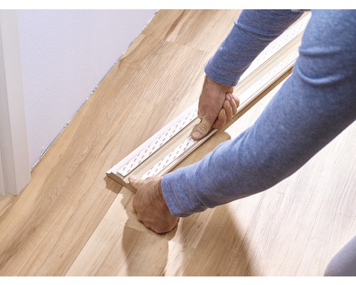 Personne fixant une plinthe au sol avec du ruban adhésif.