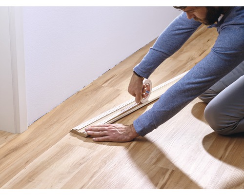 Une personne fixe une plinthe avec du ruban adhésif sur un plancher en bois.