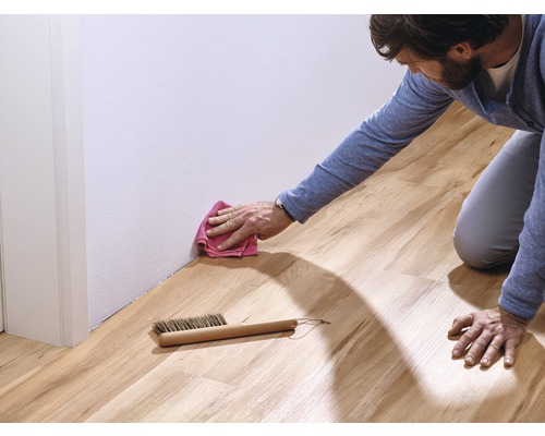 Un homme nettoie un sol stratifié avec un chiffon et une brosse le long d''un mur blanc