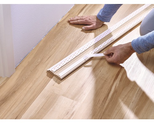 Fixation d''une plinthe avec du ruban adhésif sur un plancher en bois.