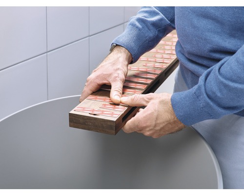 Un homme tient une planche en bois avec des bandes adhésives au-dessus d''un récipient