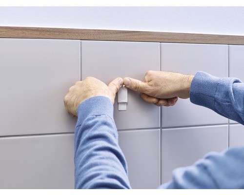 Une personne fixe un crochet sur un mur carrelé