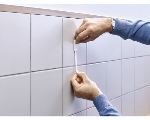 Une personne fixe une corde de carreleur sur un mur carrelé pour aligner les carreaux.