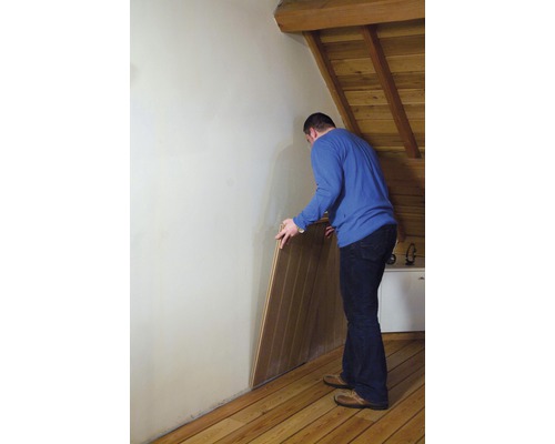 Un homme installe des panneaux de bois sur un mur dans une pièce mansardée.