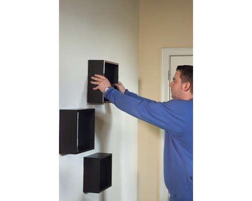 Une personne installe des étagères murales carrées sur un mur.