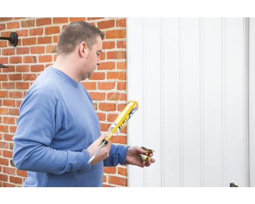 Homme avec cartouche de mastic et poignée de porte devant une porte d''entrée