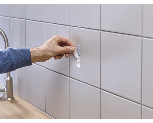 Une personne fixe une bande adhésive sur un mur carrelé.