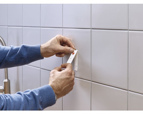 Une personne fixe un objet à un mur carrelé à l''aide d''une bande adhésive.