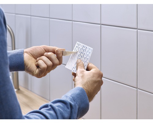 Une personne retire le film protecteur d''une bande adhésive devant un mur carrelé.