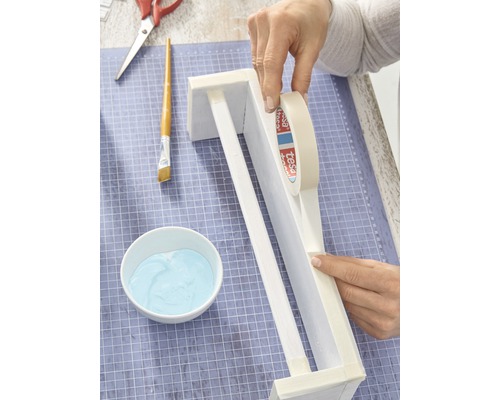 Scène de bricolage avec les mains, ruban de masquage, pinceau, peinture et ciseaux sur un tapis de découpe