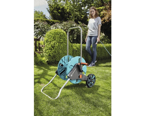 Gartenszene mit einer Frau und einem Gardena Schlauchwagen auf einer Rasenfläche