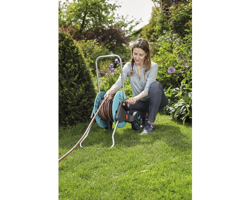 Eine Frau benutzt eine Schlauchtrommel im Garten, um einen Wasserschlauch aufzurollen.