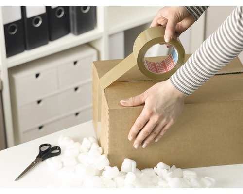 Une personne scotche un carton avec du ruban adhésif, avec des ciseaux et des chips d''emballage.
