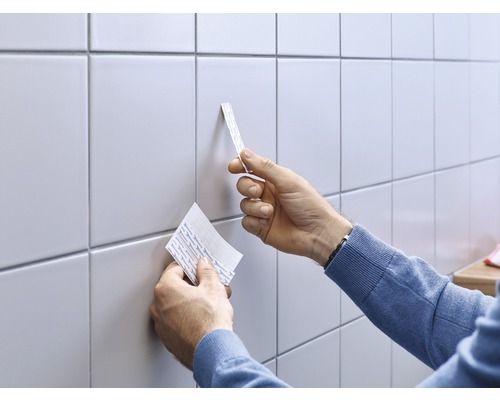 L''utilisateur pose des bandes adhésives sur du carrelage