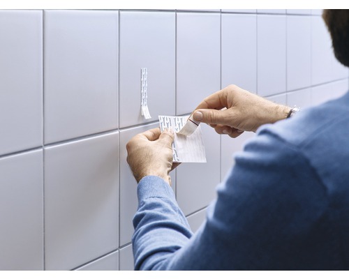 Un homme fixe des bandes adhésives sur le mur carrelé