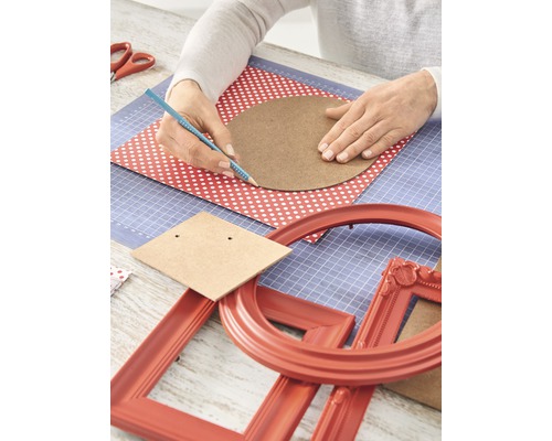Table de bricolage avec des mains dessinant un cercle sur une feuille de papier, entourée de matériel de bricolage et de cadres photo