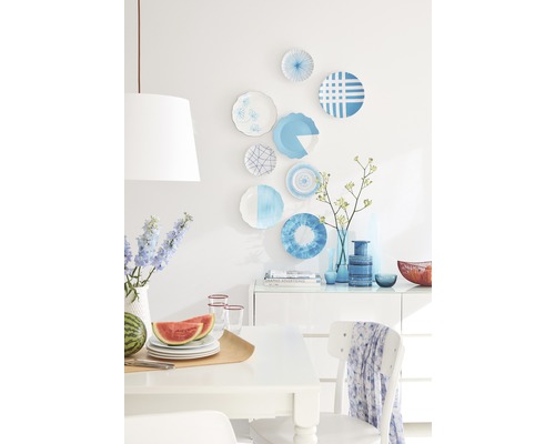 Salle à manger lumineuse avec vaisselle décorative au mur, fruits et vaisselle sur la table et vases décoratifs sur la commode.