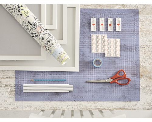 Scène avec cadres photo, rouleau de plan de ville, tapis de coupe, bandes adhésives, ruban adhésif, crayon, mètre pliant et ciseaux.