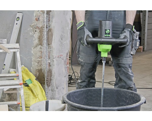 Ein Mann benutzt einen Mörtelrührer in einem Eimer auf einer Baustelle.