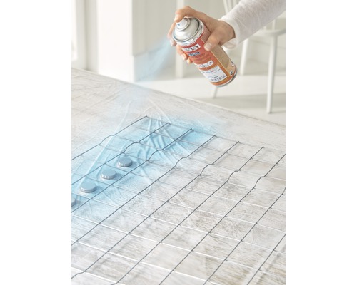 Une personne vaporise de la peinture sur une grille métallique avec un aérosol