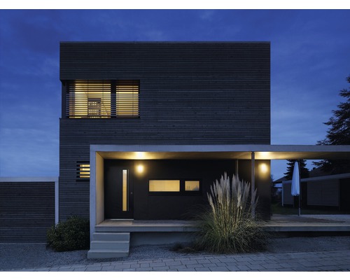 Maison moderne avec façade en bois, abri voiture et éclairage au crépuscule.
