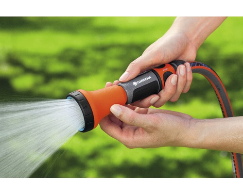 Eine Person hält einen Gartenschlauch mit Spritzdüse in der Hand, aus der Wasser strömt.