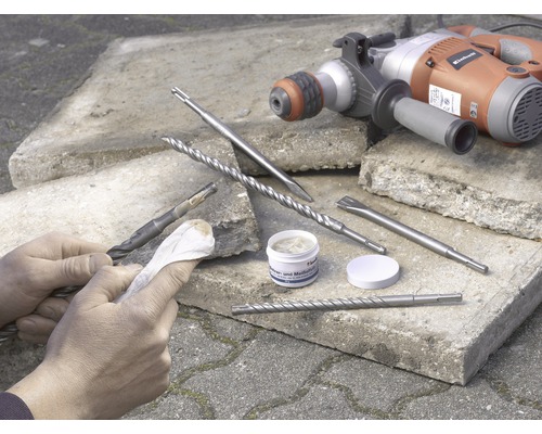 Perceuse avec forets et burins sur pierres, une personne nettoie un foret