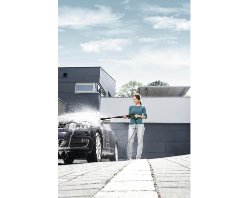 Femme nettoie voiture avec nettoyeur haute pression devant une maison