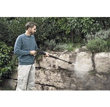 Mann reinigt Steinmauer mit einem Hochdruckreiniger im Garten.