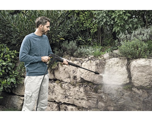 Mann reinigt Steinmauer mit einem Hochdruckreiniger im Garten.